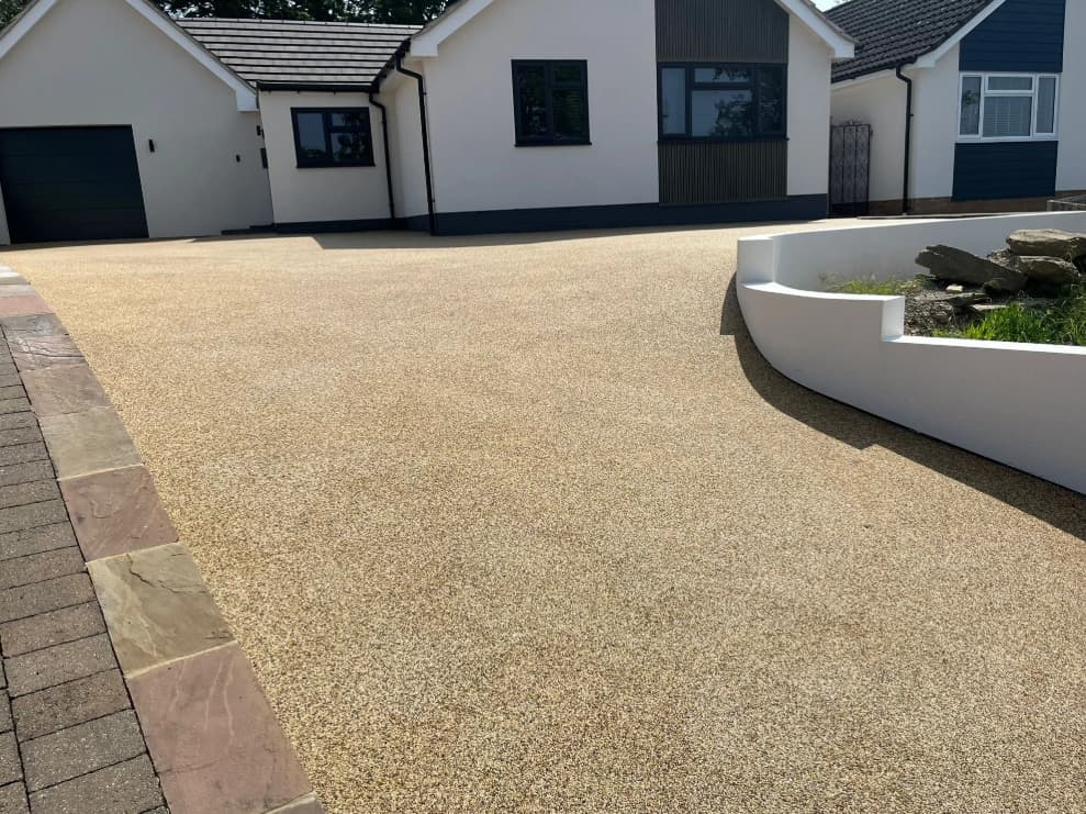 A modern house with a light-colored resin driveway, a curved white planter with rocks, and a paved path along the edge.